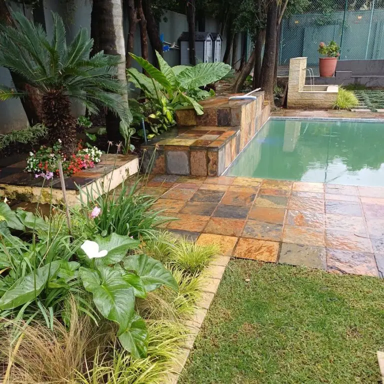 Swimming pool with natural stone paving and lush planting around the poolside area with water feature in the background
