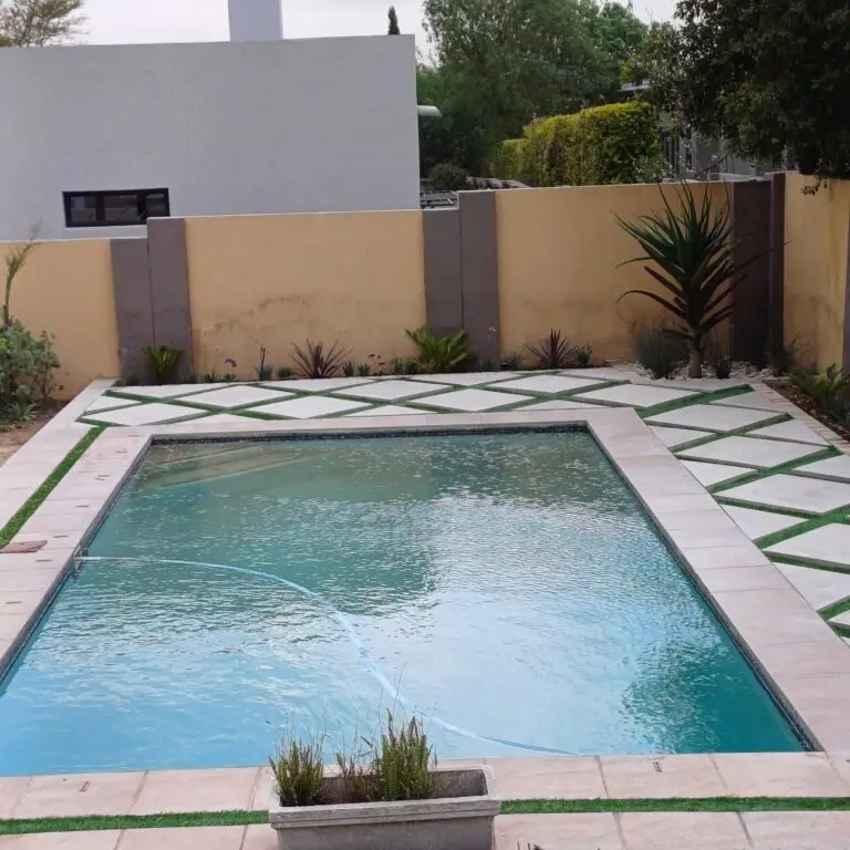 Swimming pool framed by paving, lawn and low-maintenance garden planting