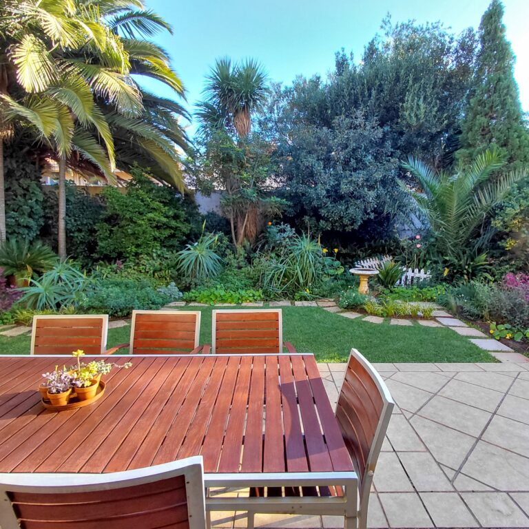 Outdoor timber dining table surrounded by lush established garden planting
